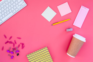 Content of student's bag. Keyboard, notebook, stationery, coffee cup on pink background top view copy space