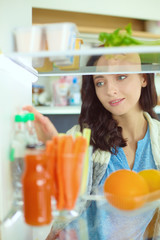 Portrait of female standing near open fridge full of healthy food, vegetables and fruits. Portrait of female