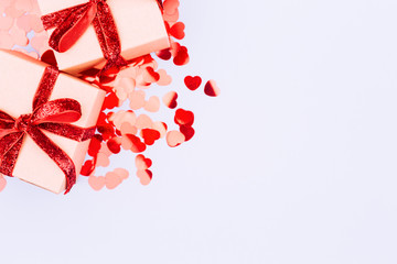 Craft boxes with red ribbon bow and glitter heart confetti. Valentine day concept. Trendy minimalistic flat lay design background