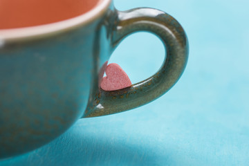 Small Pink Red Heart Shape Sugar Candy on the Handle of Coffee Tea Cup on Light Blue Background. Valentines Mothers Day Charity Concept.Greeting Card Poster Template with Copy Space for Text Lettering