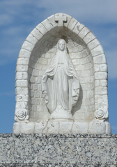 Small statuette of Blessed Virgin Mary in alcove as memorial on gravestone