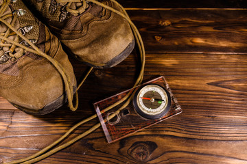 Touristic magnetic compass and boots on wooden table