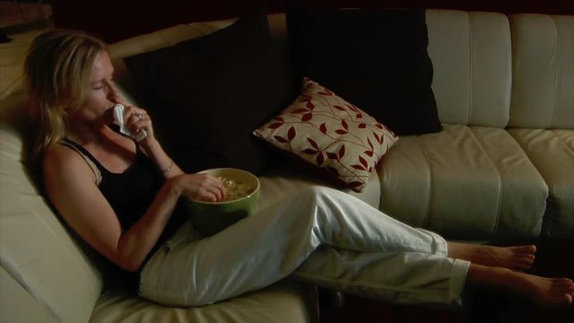 Pretty woman watching movie eating popcorn dabs tears from eyes