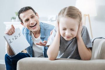 Hot-tempered. Resentful dark-haired young father holding and pointing at his daughters incorrect equation and shouting at her