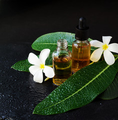 small glass jars with oil and Frangipani Plumeria patchouli flowers for spa treatments black background, selective focus - obrazy, fototapety, plakaty