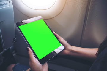 Mockup image of a woman holding and looking at black tablet pc with blank green desktop screen next to an airplane window