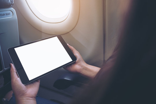 Mockup image of a woman holding and looking at black tablet pc with blank white desktop screen next to an airplane window