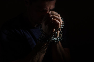 Repented man prisoner with his hands shackled in chains on a dark background