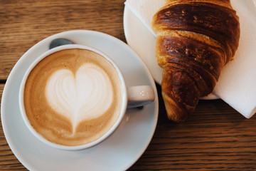 Coffee with latte art heart and fresh baked croissant