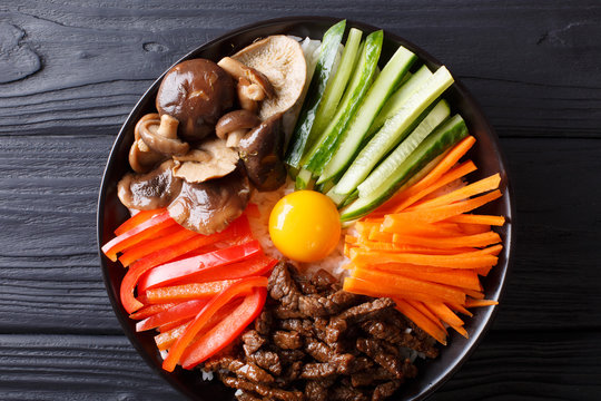 Korean healthy food Bibimbap of rice with fried beef, raw egg, vegetables, shiitake close-up in a bowl. Horizontal top view