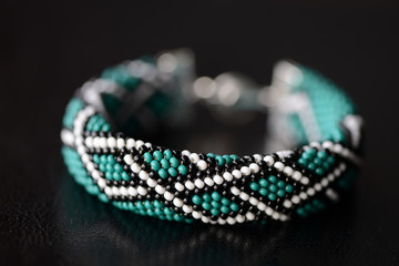 Green bead crochet bracelet with celtic print on a dark background close up
