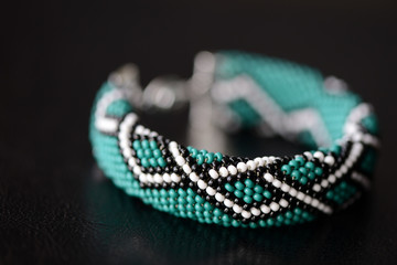 Green bead crochet bracelet with celtic print on a dark background close up