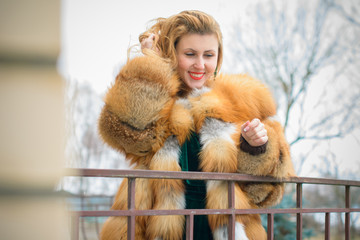 Young lady in fox fur jacket and velvet dress, vintage elegant style in everyday life, retro 50h lifestyle for women. Pretty woman outdoor on a balcony at nature view 