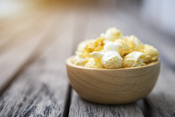 Closeup salted popcorn in round wooden bowl on wooden floor with vintage flare light, movie night snack