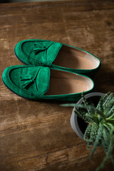 Green man&rsquo;s shoes on a wooden floor near standing a pot with aloe out of focus