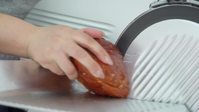 Electric food slicer. Meat slicing machine cutting processed meat products. Stainless steel blade slices smoked and cured pork bacon. Woman chef cuts pork loin.