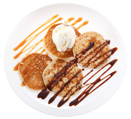 Serving pancakes with ice cream on the plate. Decorated with chocolate syrup and caramel syrup. Isolated on white background. Top view.