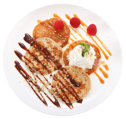 Serving pancakes with ice cream on the plate. Decorated with chocolate syrup, caramel syrup, fresh berries and mint. Isolated on white background. Top view..