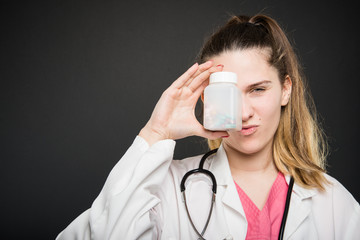 Attractive female doctor covering eye with bottle of pills