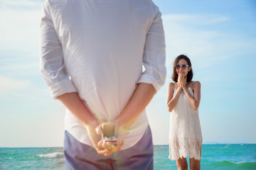 man making proposal with engagement ring and gift box to his woman at sea beach - wedding concept