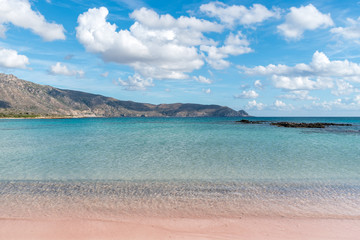 Soft waves of the sea on the pink sand and beautiful beach with cliffs.Coast of Crete island in Greece. Pink sand beach of famous Elafonisi