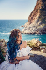Fototapeta na wymiar Young woman standing on cliff's edge and looking into a wide sea view. Wind Long Blue hair hairstyle.