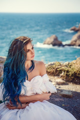 Fototapeta na wymiar Young woman standing on cliff's edge and looking into a wide sea view. Wind Long Blue hair hairstyle.