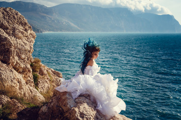 Young woman standing on cliff's edge and looking into a wide sea view. Wind Long Blue hair hairstyle.