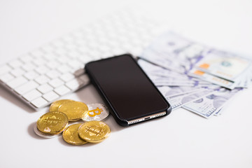 Bitcoin golden coins on a dollar banknotes. Office background. White keyboard, mobile phone, and money. Money balance. Investment risk. Cryptocurrency