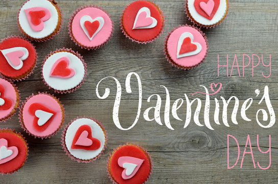 HAPPY VALENTINE’S DAY card with cupcakes decorated with hearts arranged on wooden background