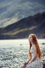 Fototapeta na wymiar Young red-haired girl in the style of Boho. Enjoys the beauty of the sea coast. The idea and concept of freedom and hippies