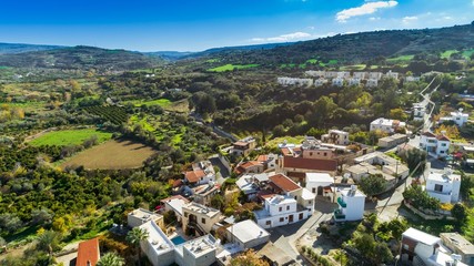 Fototapeta premium Aerial bird eye view of Goudi village in Polis Chrysochous valley, Paphos, Cyprus. View of traditional ceramic tile roof houses, church, trees, hills and Akamas - Latchi beach bay from above.