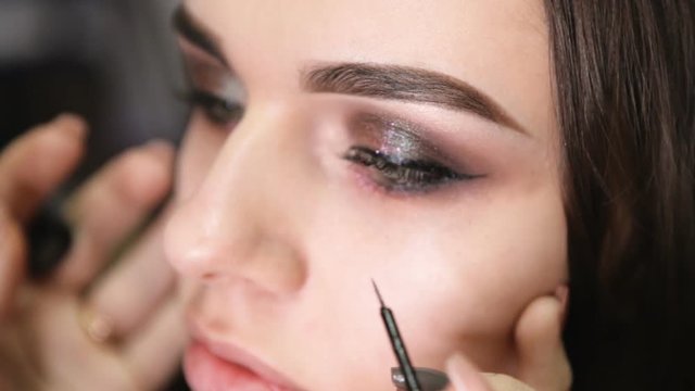 make-up artist draws arrows on the girl's eye