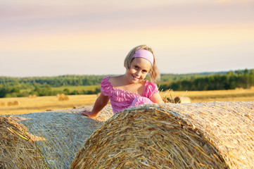 Naklejka na ściany i meble Cheerful little girl in field on straw rolls