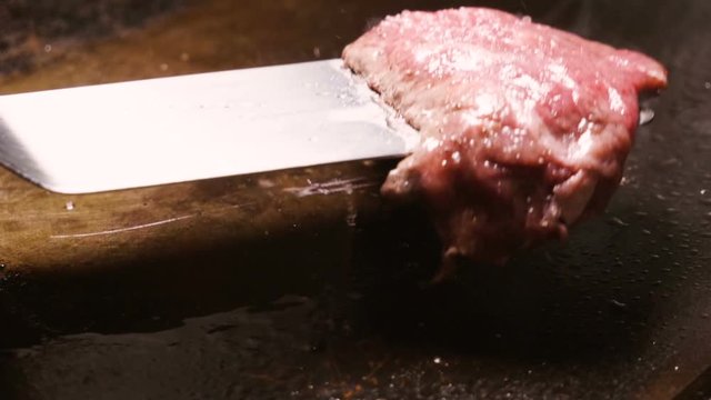 Close-up shot of cook turning over one chicken breast frying on grill pan. Slow motion. HD