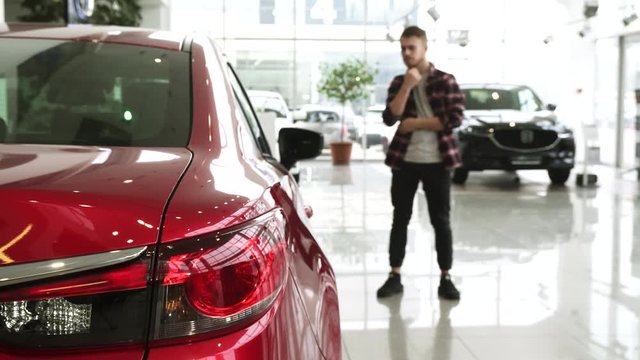 Male customer rubbing beard thoughtfully choosing a new car at the dealership