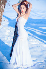 Fototapeta na wymiar Lady in white long dress. Pretty young elegant and sexy woman posing in wedding dress in rustic style, on winter snow. Magical Wedding in winter time 