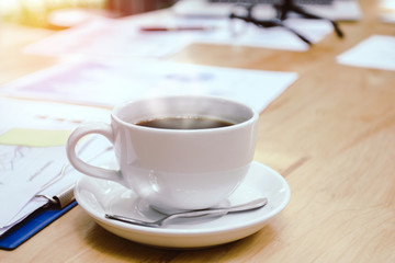 Cup of white coffee with smoke. folders and documents on  desk with glasses and laptop