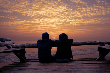 Couple relaxing on wooden terrace and looking to Sunrise on the beach.