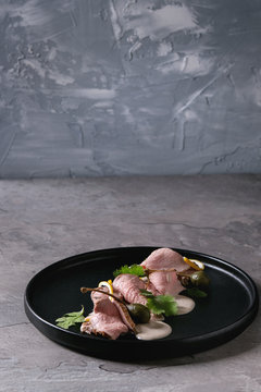 Fototapeta Vitello tonnato italian dish. Thin sliced veal with tuna sauce, capers and coriander served on black plate over gray texture kitchen table.