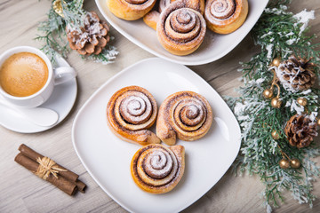 Fresh homemade buns with cinnamon, a cup of coffee, cinnamon sticks. Selective focus, close-up