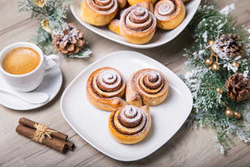 Fresh homemade buns with cinnamon, a cup of coffee, cinnamon sticks. Selective focus, close-up