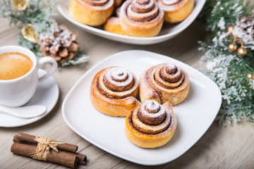 Fresh homemade buns with cinnamon, a cup of coffee, cinnamon sticks. Selective focus, close-up