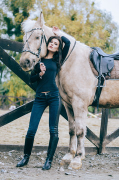 Beautiful brunette posing with a horse in the autumn afternoon. Lifestyle Photo. Fashion photo. Horseback riding