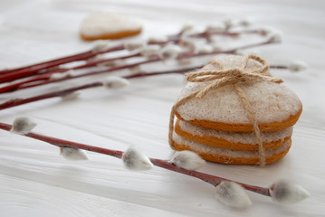 Fototapeta premium Spring background. Pussy willow twigs and heart shaped gingerbread cookies on white wooden board. Selective focus.