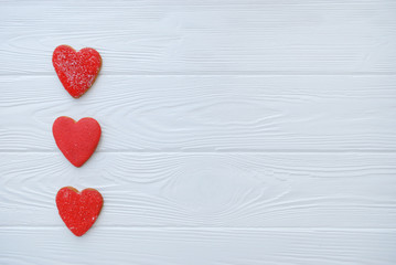 Three gingerbread heart shaped red cookies on white wooden background. Valentine's day or love...