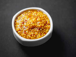 Grain mustard on gravy boat at black background