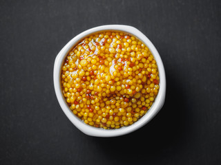 Grain mustard on gravy boat at black background