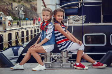 A beautiful little girl girlfriend in a marine style against the backdrop of boats and yachts. Idea and concept Friendship, vacations, rest