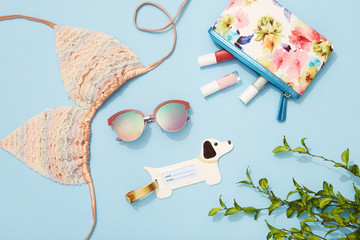 Beach holiday accessories, bikini, sunglasses, makeup bag on blue background, travel flat lay